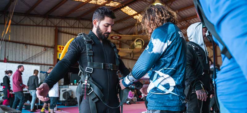 Skydiving instructor fitting harness on tandem passenger
