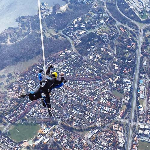 Tandem skydiving pair in freefall over Canberra with Parlamient House in the background