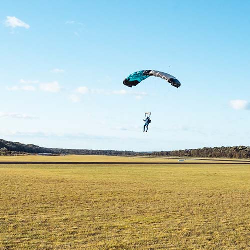 Skydiver landing on grassy field with parachute