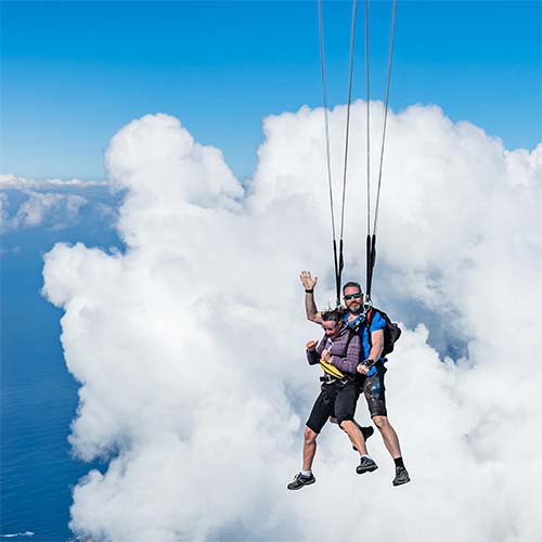 Parachutist descending through fluffy white clouds over Moruya landscape