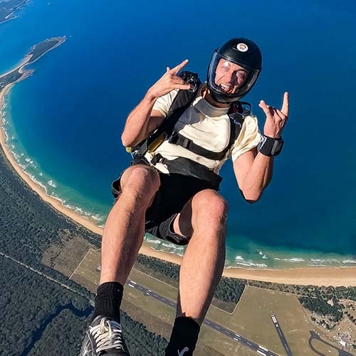 Solo skydiver giving thumbs up above Moruya's curved coastline and beaches