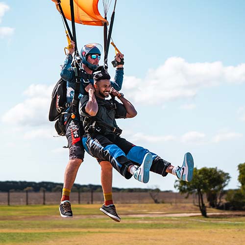 Tandem skydivers land on grassy field, instructor guiding the descent