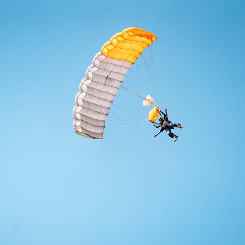 Skydiver descends under an open yellow parachute against a blue sky over Torquay
